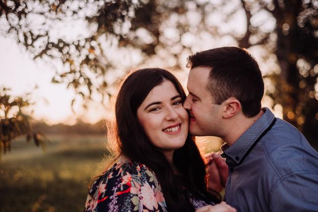 Man kissing his partner on the cheek as she smiles at the camera during a couples photography session at Perry's Paddock, Perth