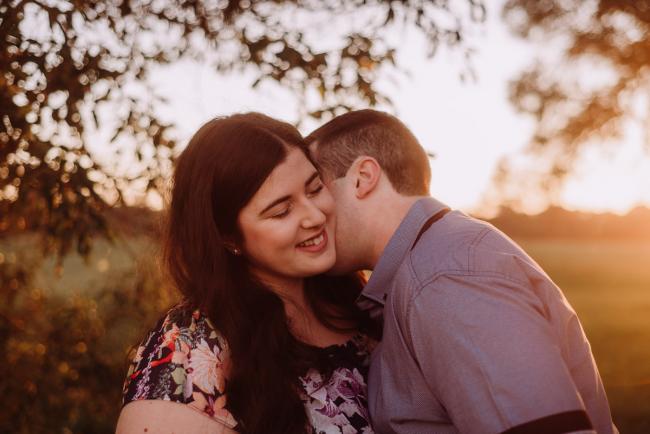 Man kisses his partner's neck as she looks down and smiles during a couples photography session at Perry's Paddock, Perth