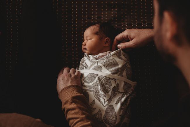 New wrapped baby laying on bed with mum and dad's hands around her during Perth Fresh 48 session