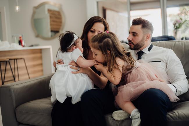 20180930-DSC_9607 Family sitting on the couch as daughter kisses the hand of her baby sister during events photography Perth session