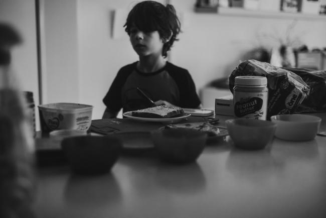 black and white photo of boy standing in the kitchen with breakfast by family photographer perth