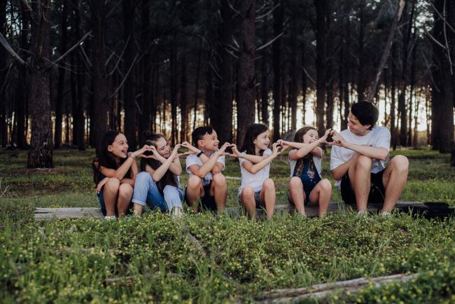 20181005-DSC_0790 Cousins sitting on a log and making a chain of love hearts with their hands during Perth family photography session at The Pines Wanneroo