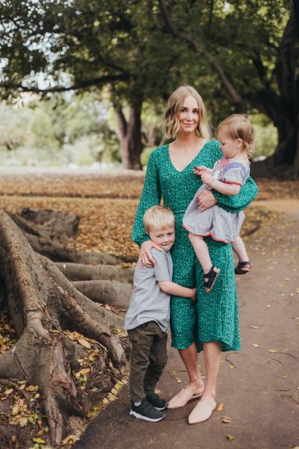 Mother carrying her daughter whilst her son wraps his arms around her leg during a family photography session at Hyde Park in Perth