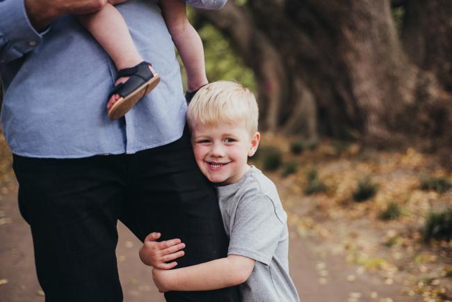 Son hugging his dad's leg during a family photography session at Hyde Park in Perth