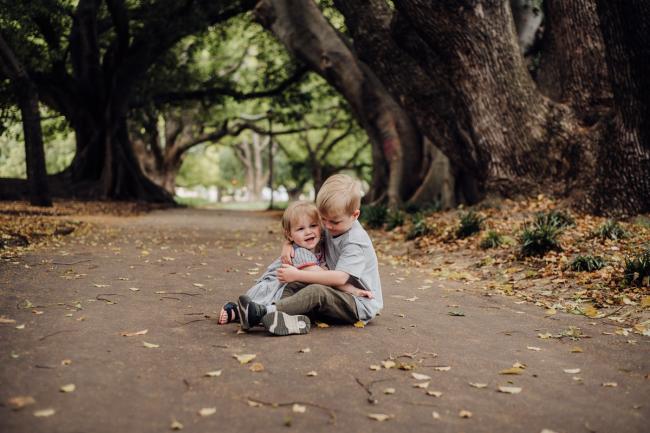 Brother and sister sitting and hugging during a family photography session at Hyde Park in Perth