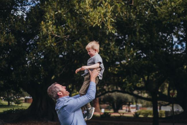 Father lifting his son into the air during a family photography session at Hyde Park in Perth