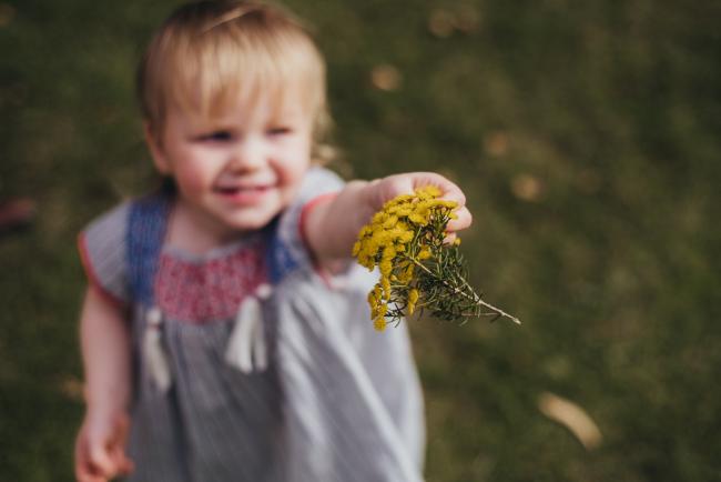 Little girl holding out yellow flowers to the camera during a family photography session at Hyde Park in Perth