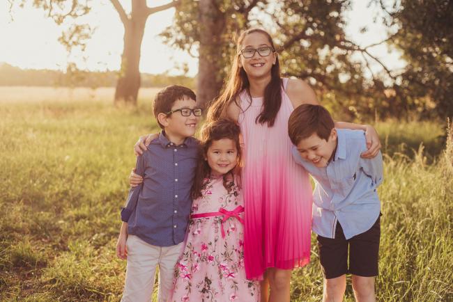 Four siblings standing with their arms around each other during a golden hour family photography session at Perry's Paddock in Perth