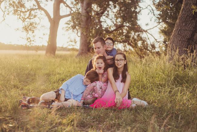 Father and his four children sitting on the grass during a golden hour family photography session at Perry's Paddock in Perth