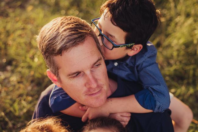 Boy hugging his dad from behind and kissing his head during a golden hour family photography session at Perry's Paddock in Perth