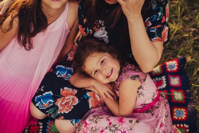 Little girl laying across her mothers lap and smiling during a golden hour family photography session at Perry's Paddock in Perth