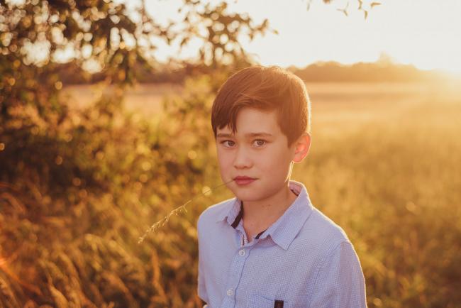 Boy looking seriously at the camera with a plant in his mouth during a golden hour family photography session at Perry's Paddock in Perth