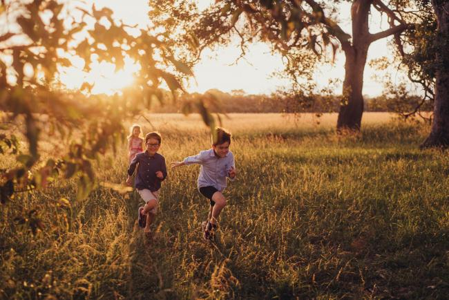 Two brothers and a sister running in the field during a golden hour family photography session at Perry's Paddock in Perth
