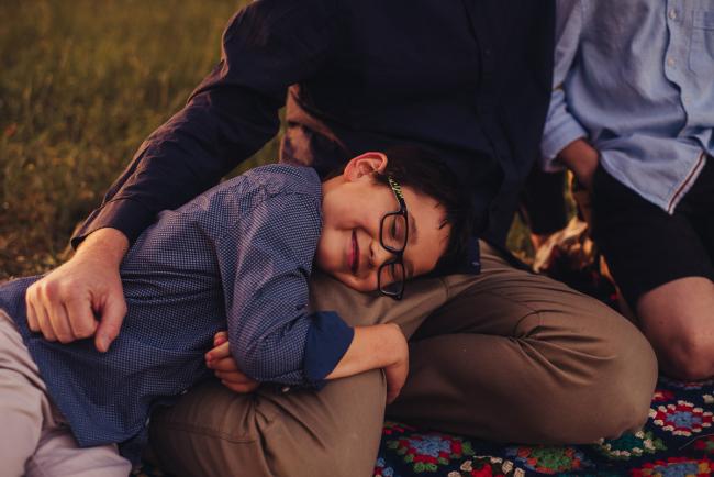 Little boy laying across his dad's lap and smiling during a golden hour family photography session at Perry's Paddock in Perth