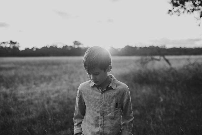 Black and white image of a little boy looking down in a field during a golden hour family photography session at Perry's Paddock in Perth