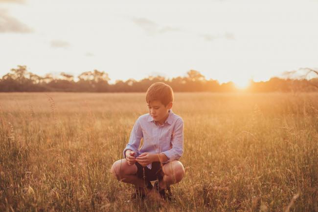 Little boy squatting in a field during a golden hour family photography session at Perry's Paddock in Perth