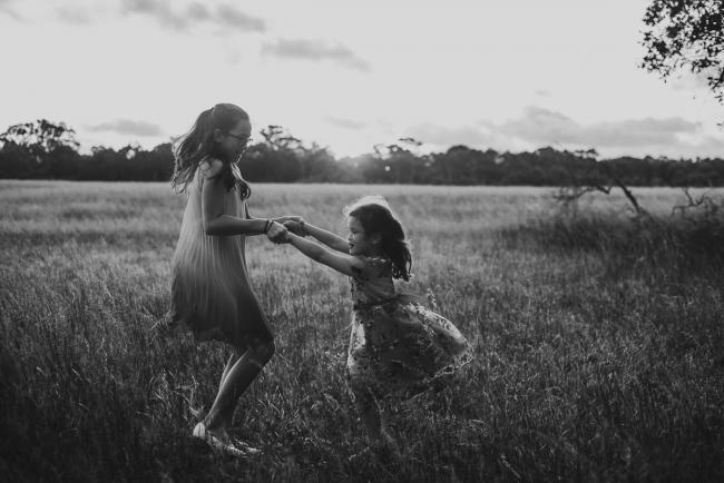Black and white image of two sisters dancing in a field during a golden hour family photography session at Perry's Paddock in Perth