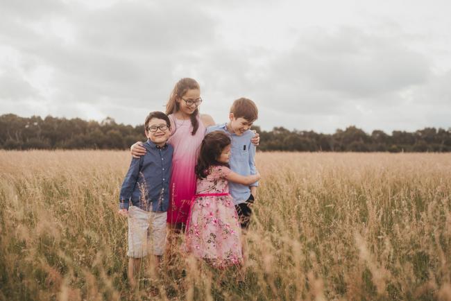 Four siblings standing in a field during a golden hour family photography session at Perry's Paddock in Perth