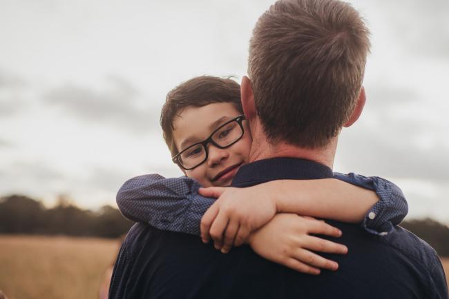 Little boy facing the camera with his arms wrapped around his dad's neck during a golden hour family photography session at Perry's Paddock in Perth