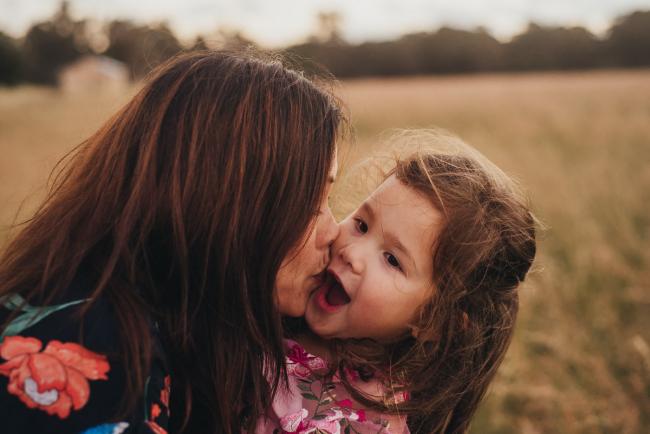 Mother kissing her daughter during a golden hour family photography session at Perry's Paddock in Perth