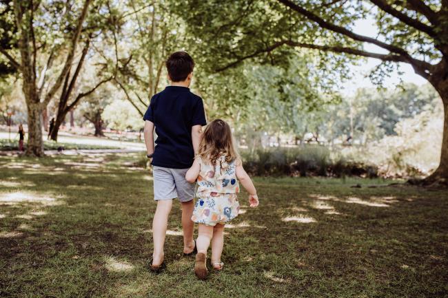 Big brother and little sister holding hands and walking away during a mini session with Perth family photographer at Hyde Park