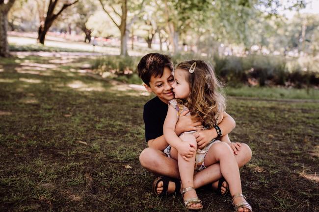 Little sister sitting on her big brothers lap during a mini session with Perth family photographer at Hyde Park