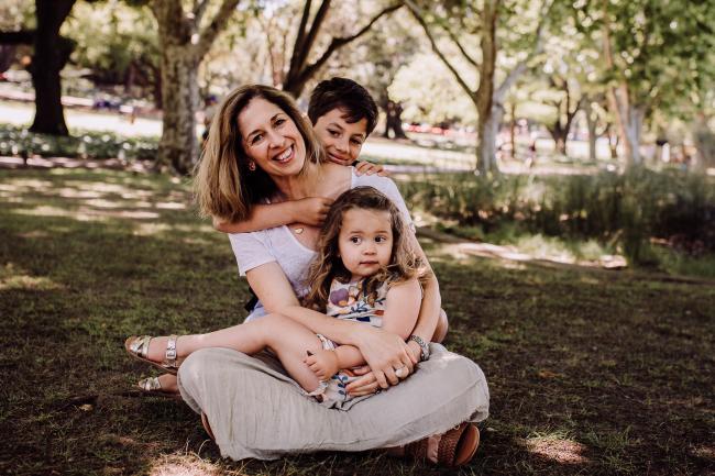 Mother sitting with her daughter on her lap and her son hugging her from behind during a mini session with Perth family photographer at Hyde Park