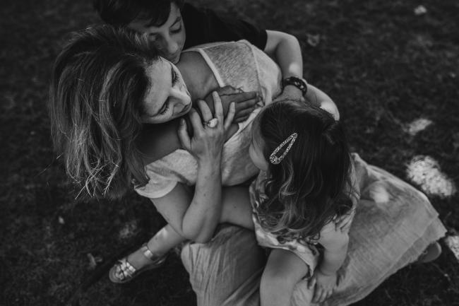 Black and white image of a little girl sitting on her mother's lap, and a little boy hugging his mother from behind during a mini session with Perth family photographer at Hyde Park