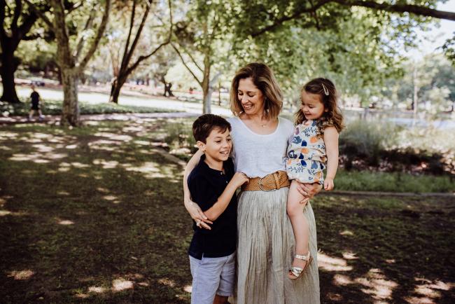Mother standing holding her daughter and her arm around her son during a mini session with Perth family photographer at Hyde Park