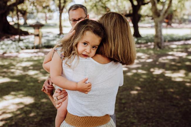 Little girl being carried and hugged by her mother during a mini session with Perth family photographer at Hyde Park