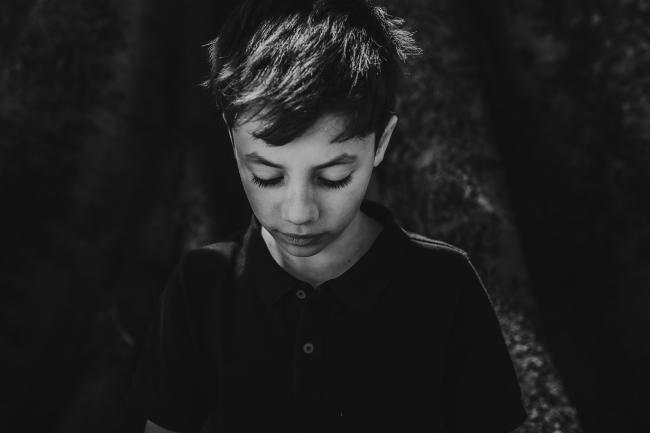 Black and white image of little boy looking down during a mini session with Perth family photographer at Hyde Park