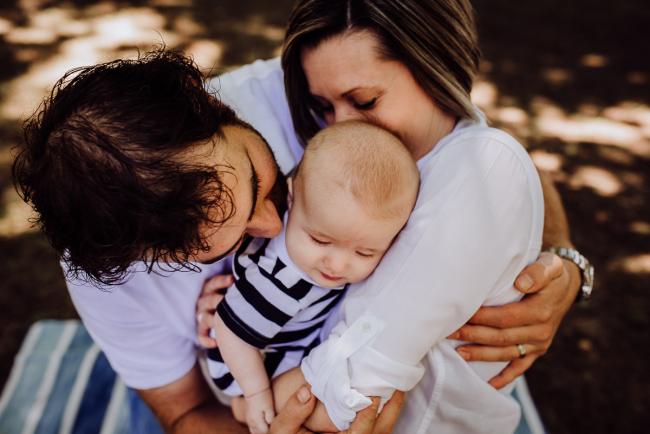 Mother and father hugging each other and their baby during a family photography session in Hyde Park, Perth