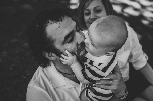 Black and white image of a baby son grabbing onto his fathers face during a mini session with Perth family photographer at Hyde Park