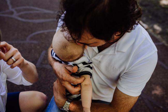 Top down shot of father hugging his baby son to his chest during a mini session with Perth family photographer at Hyde Park