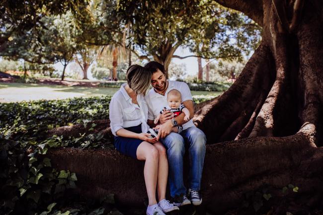 Mother and father sitting on a tree branch with their baby son during a mini session with Perth family photographer at Hyde Park