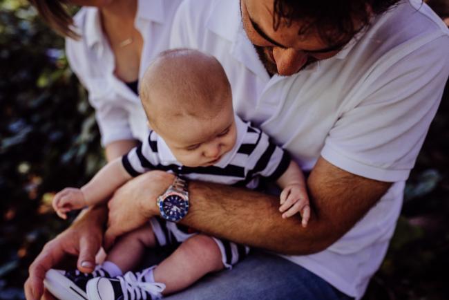 Father holding his baby son on his lap during a mini session with Perth family photographer at Hyde Park