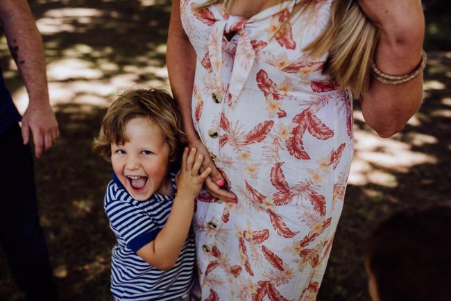 Little boy holding onto his mothers hand and dress during a family photography session in Hyde Park, Perth