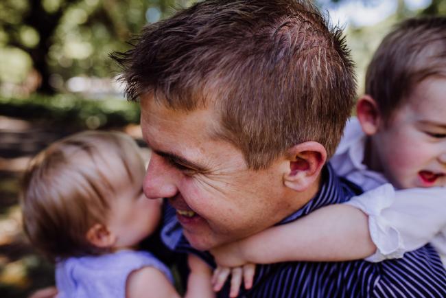 Close up of dad carrying his daughter with his son wrapped around his neck during a mini session with Perth family photographer at Hyde Park