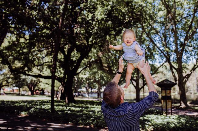 Little girl being thrown in the air by her dad during a mini session with Perth family photographer at Hyde Park