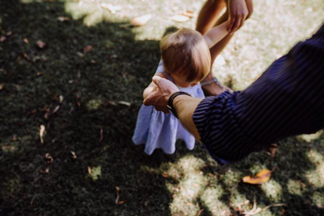 Little girl learning to walk as being held by her mum and dad during a mini session with Perth family photographer at Hyde Park