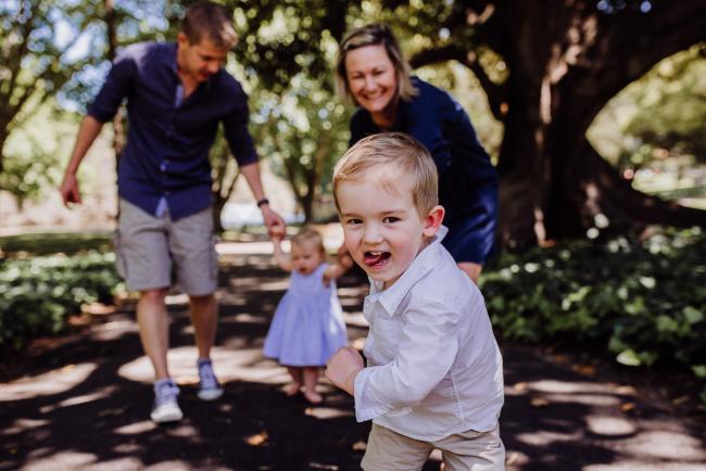 Little boy leading his family in a game of 'follow the leader' during a family photography session in Hyde Park, Perth