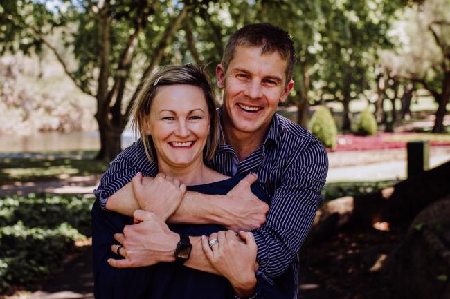 Couple smiling with the man hugging the woman from behind during a mini session with Perth family photographer at Hyde Park