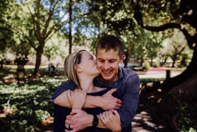 Woman leaning back and kissing her husband as he laughs during a Perth family session at Hyde Park