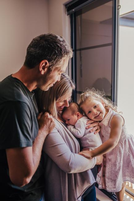 20181111-DSC_8278-2 Mum and dad holding their new baby by the window with their daughter cuddling into them in a lifestyle family photography session Perth