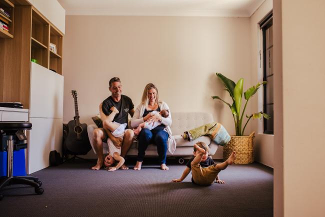 20181111-DSC_8330 Family sitting on a couch with their new baby, their daughter upside down and their son rolling on the floor in a lifestyle family photography session Perth