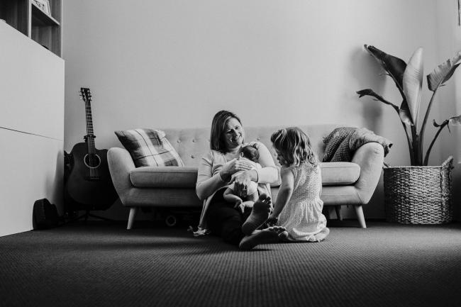 20181111-DSC_8407-1 black and white image of a mother sitting on the floor with her daughter and her new baby in a lifestyle family photography session Perth