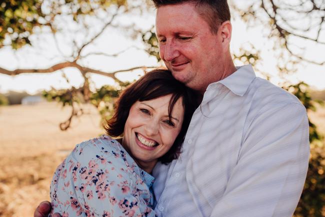 Woman smiling and resting her head on her husband's chest during an extended family photography session at Perry's Paddock in Perth