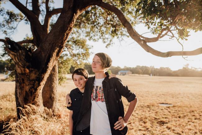 Two brothers with their arms around each other under a tree during an extended family photography session at Perry's Paddock in Perth