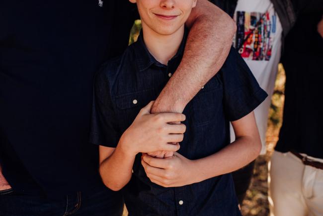 Boy holding onto his fathers hand which is wrapped around his shoulders during an extended family photography session at Perry's Paddock in Perth