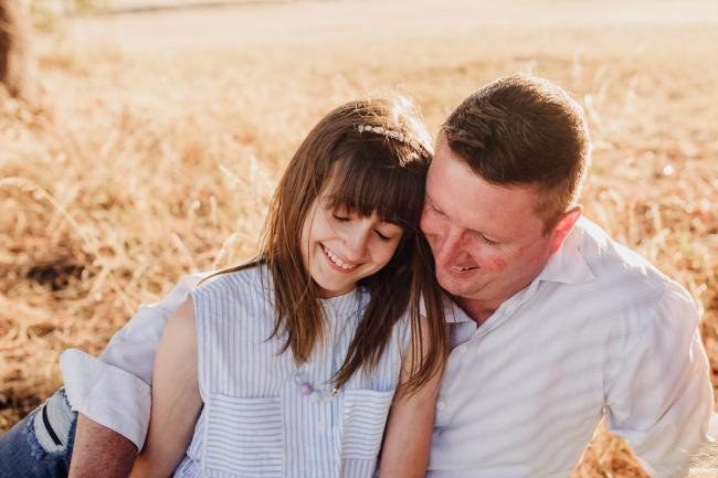 Girl smiling and leaning into her father during an extended family photography session at Perry's Paddock in Perth